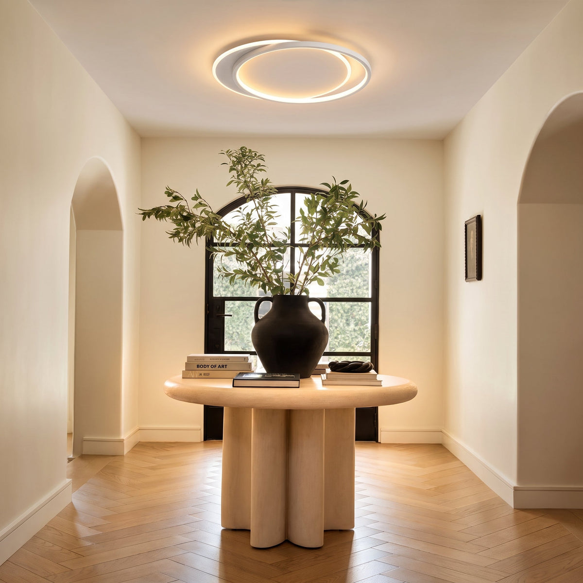 Ring light above a round pale wood table holding a black vase and books 6