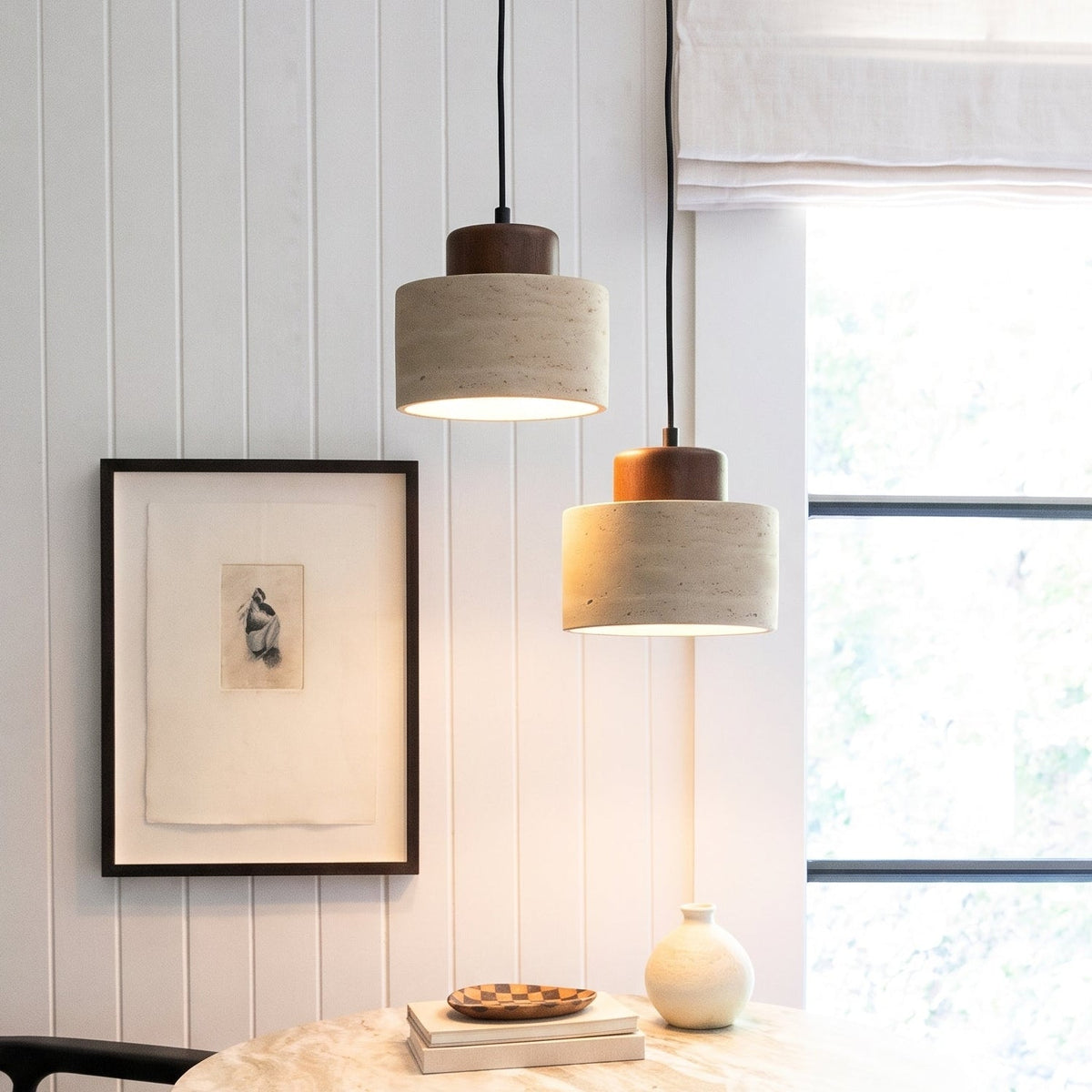 Two lit pendant lights hang beside a window above a marble table and a panelled wall 1