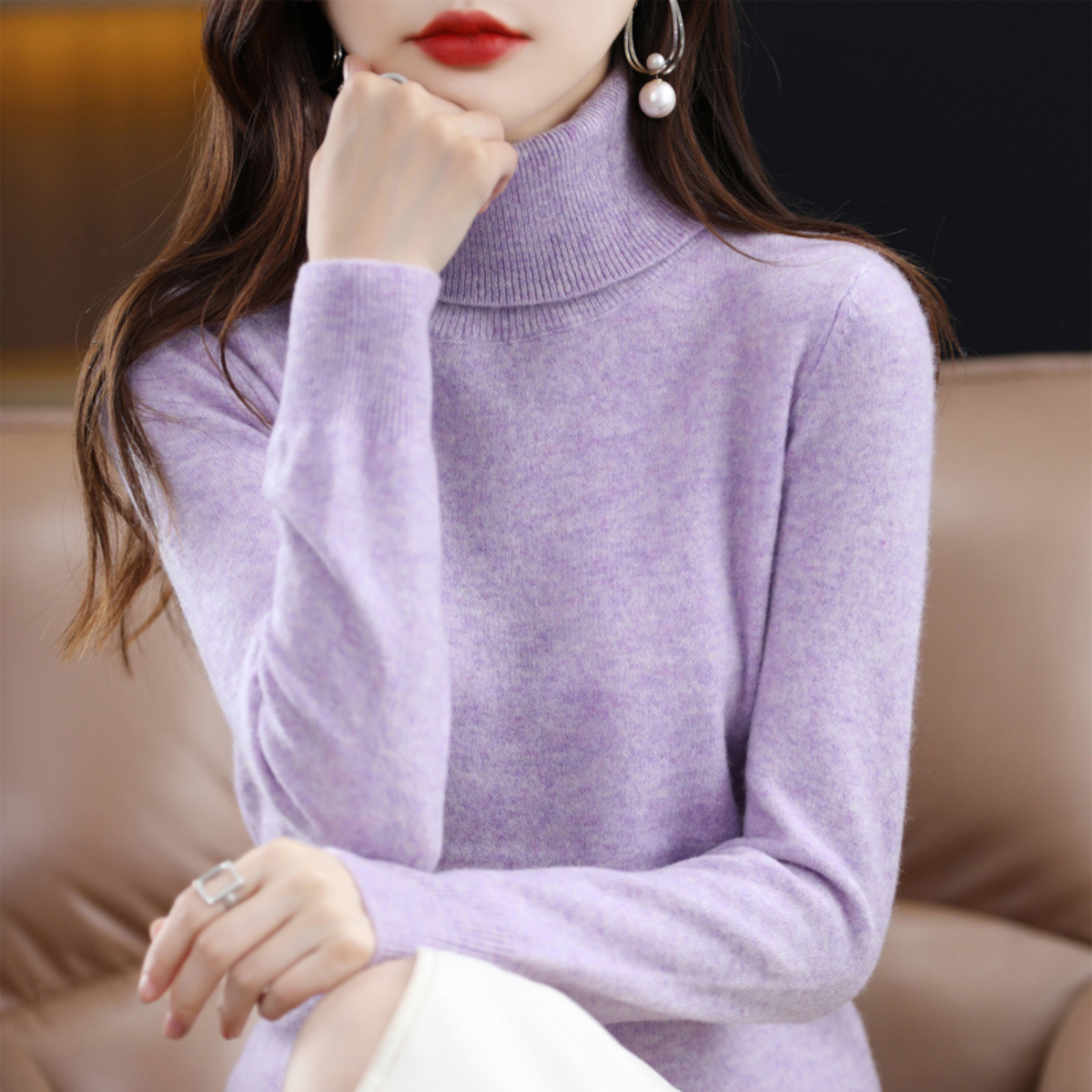 Soft lilac marl roll-neck jumper on a seated model with her hand raised to her chin, showing the ribbed fold-over collar. 6