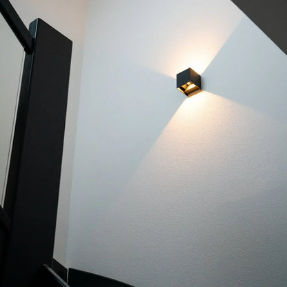Black cube light on a white textured wall beside a staircase balustrade, seen from below 8
