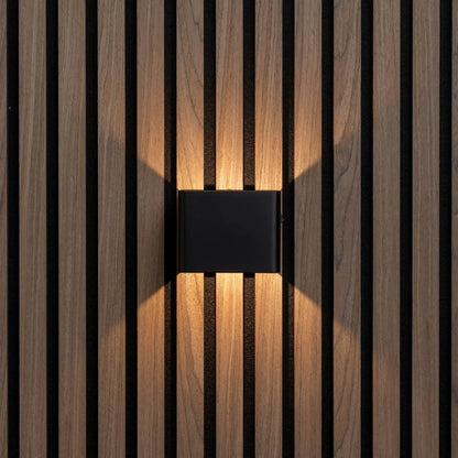 Front view of the black cube light casting warm light up and down a slatted wall 5