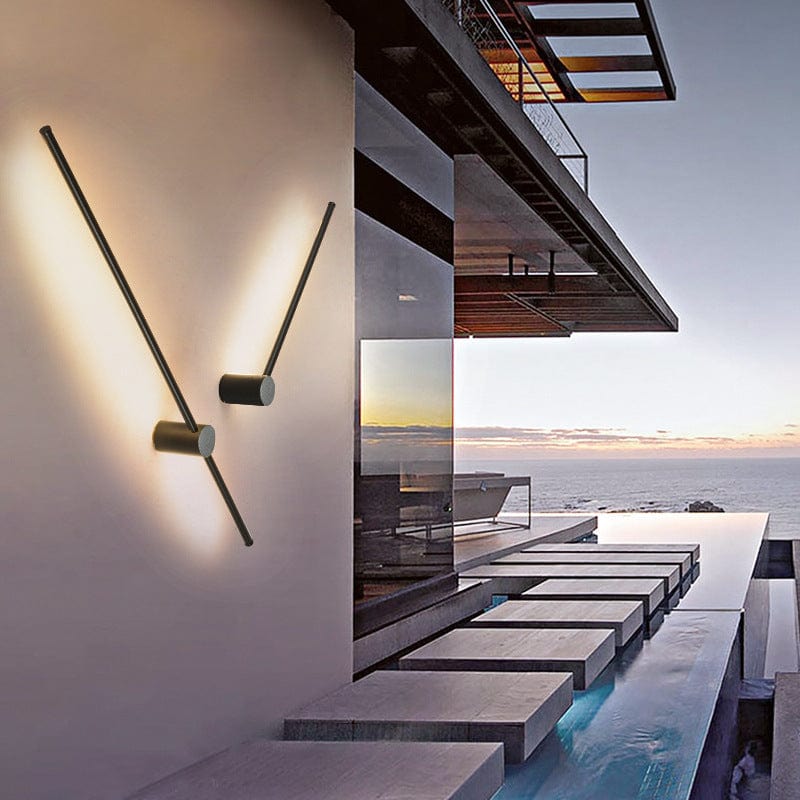 Two black light bars angled in a V on a smooth wall, casting warm light beside a modern pool terrace at sunset. 2