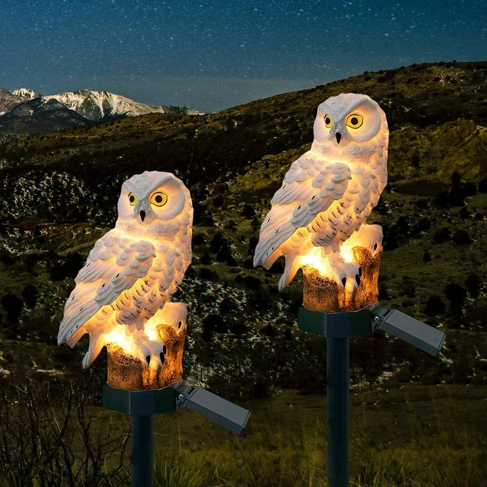 Two white owl lights glowing on stakes in a hillside garden under a starry night sky. 4