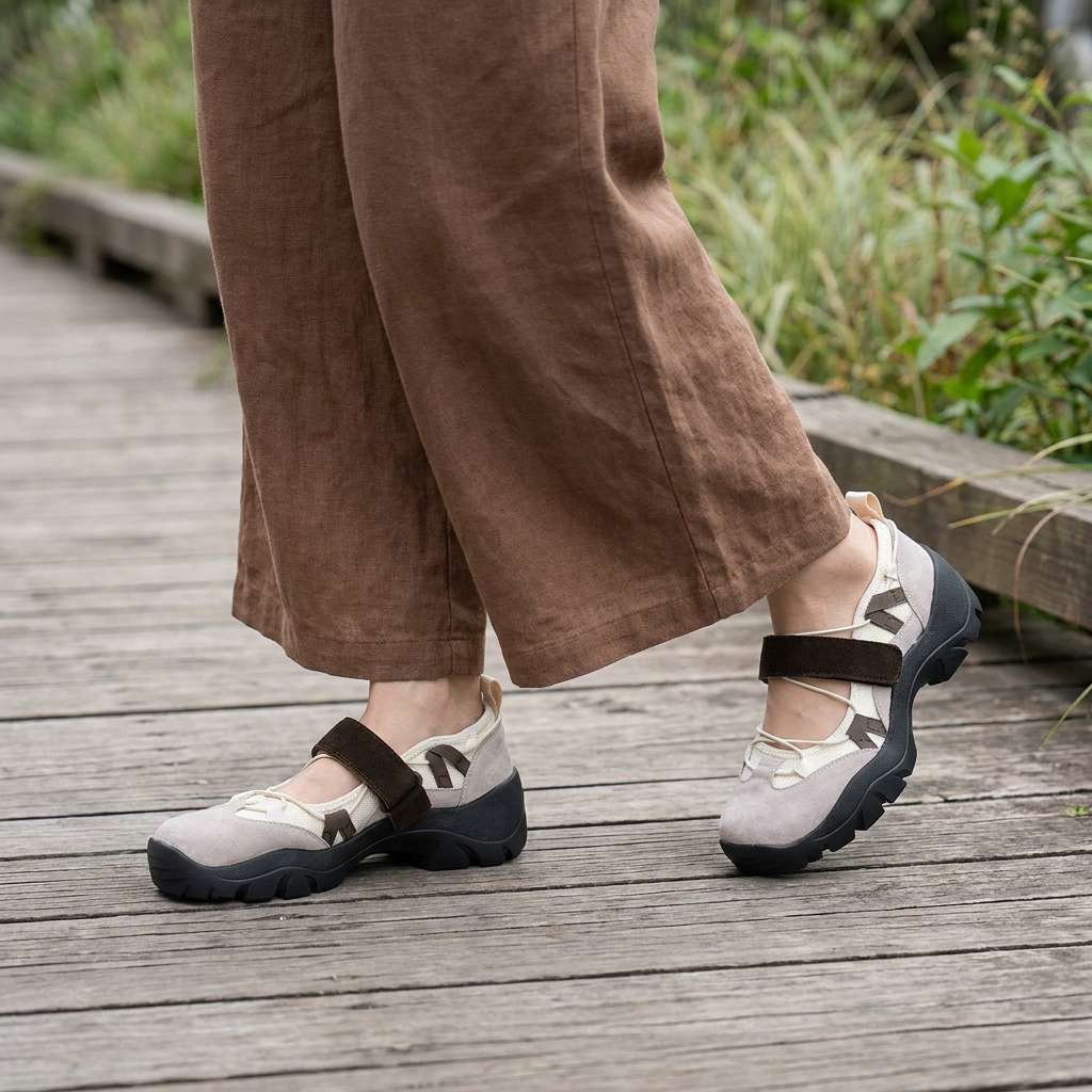 Taupe suede shoes with brown straps and black soles, worn with brown linen wide-leg trousers on a wooden boardwalk. 11
