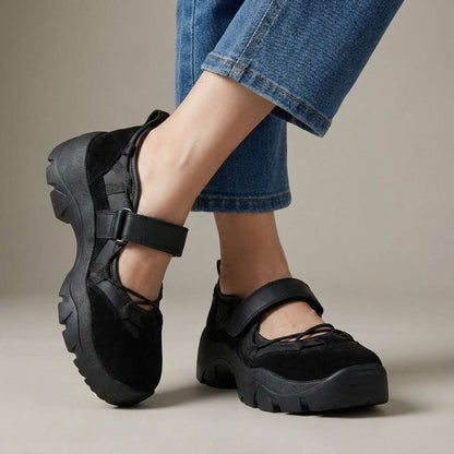 Studio shot of all-black suede shoes with a black strap and chunky black sole, worn with wide-leg blue jeans. 5