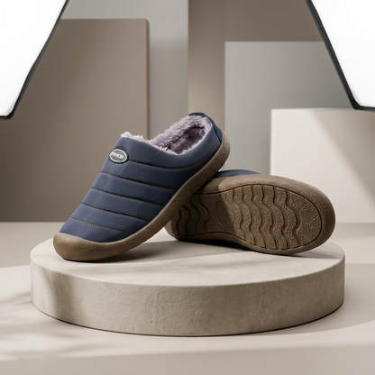 Navy quilted slippers with soft grey fleece lining, one resting on its side to show the wavy tread sole 1