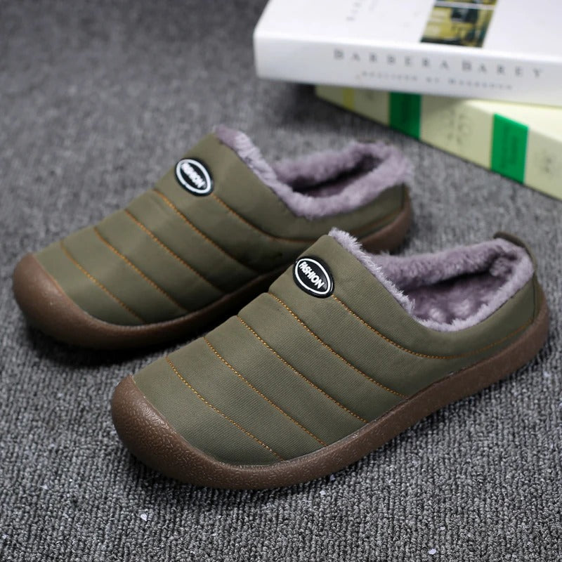 Pair of olive green quilted slippers with fleece lining, resting on grey carpet beside books 1