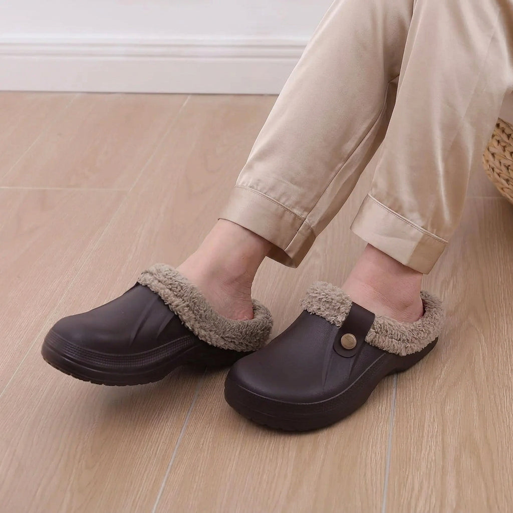 Person wearing dark brown fur-lined clogs with grey leggings, seated on a wooden floor 10