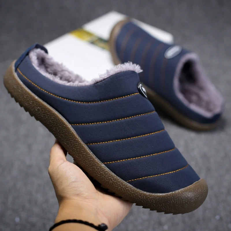 Hand holding a navy blue quilted slipper to show its fleece lining and textured sole 6