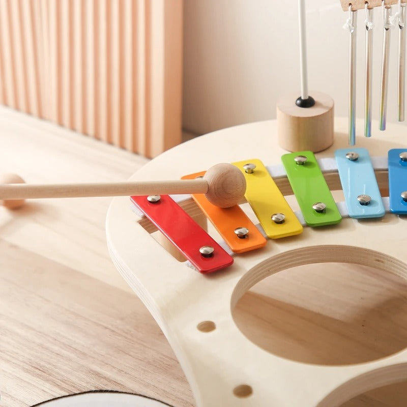 Close-up of the rainbow xylophone bars being struck with a wooden mallet, beside the drum cut-out 10