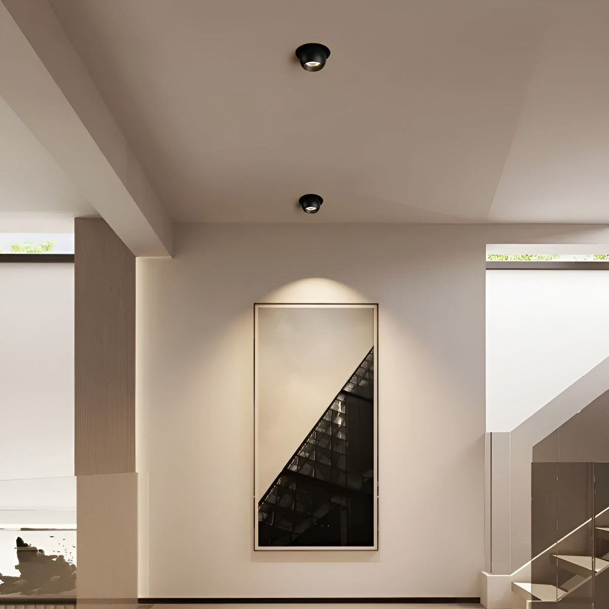 Two black recessed spotlights in a hallway ceiling, one lighting a large framed picture below 3