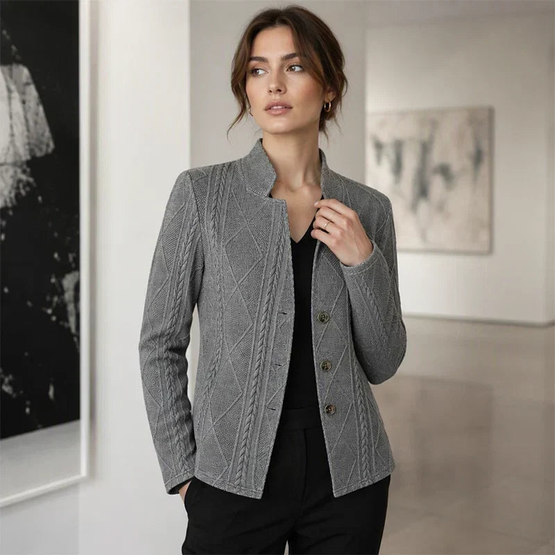 Woman in the grey textured blazer over a black top in a gallery, one hand at her collar and the other in her pocket. 11