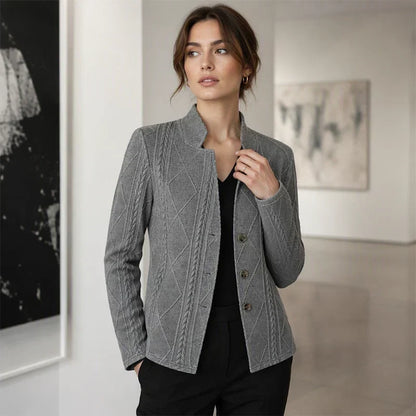 Woman in the grey textured blazer over a black top in a gallery, one hand at her collar and the other in her pocket. 11