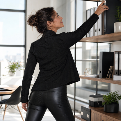 Back view of a woman in the black textured blazer and leather-look trousers, reaching up to a shelf of office files. 13
