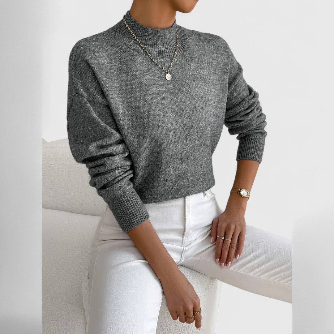 Model wearing the jumper in marl grey with white jeans and a single pendant necklace, sleeves slightly bunched at the wrist. 12