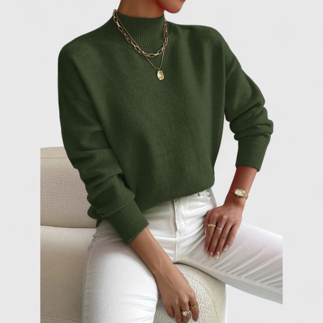 Model wearing the jumper in dark olive green with white jeans, ribbed high neck and cuffs shown. 10