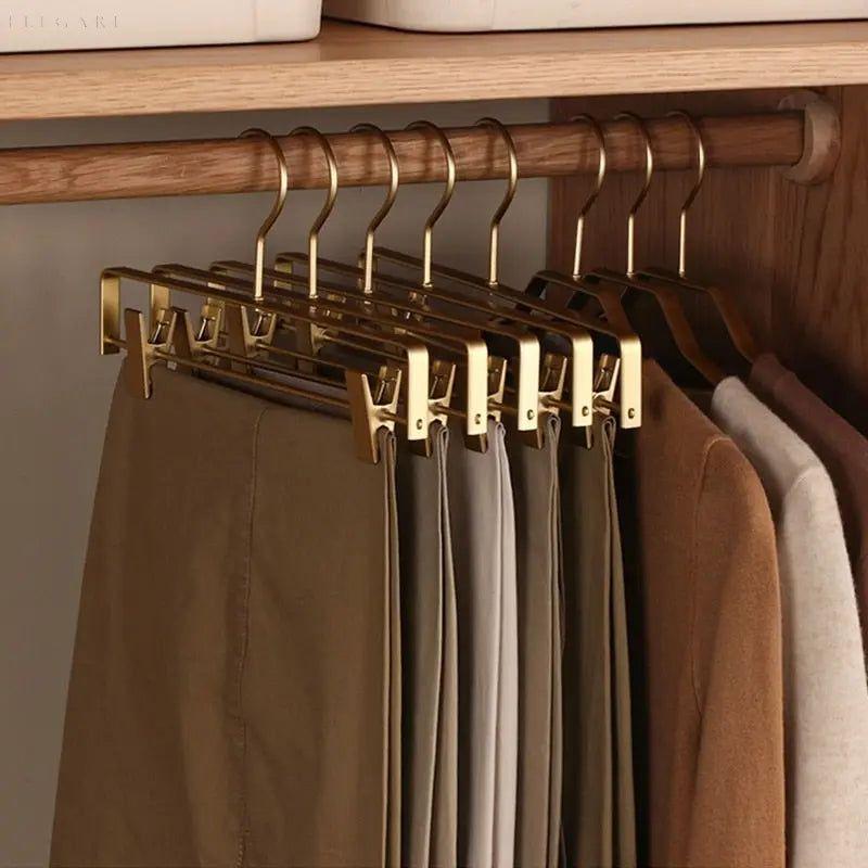Row of gold clip hangers on a wooden wardrobe rail, each holding neutral-coloured trousers 3