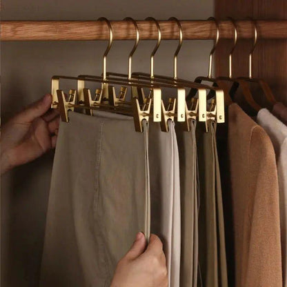 Hand sliding beige trousers along a rail of gold clip hangers in a wardrobe 7