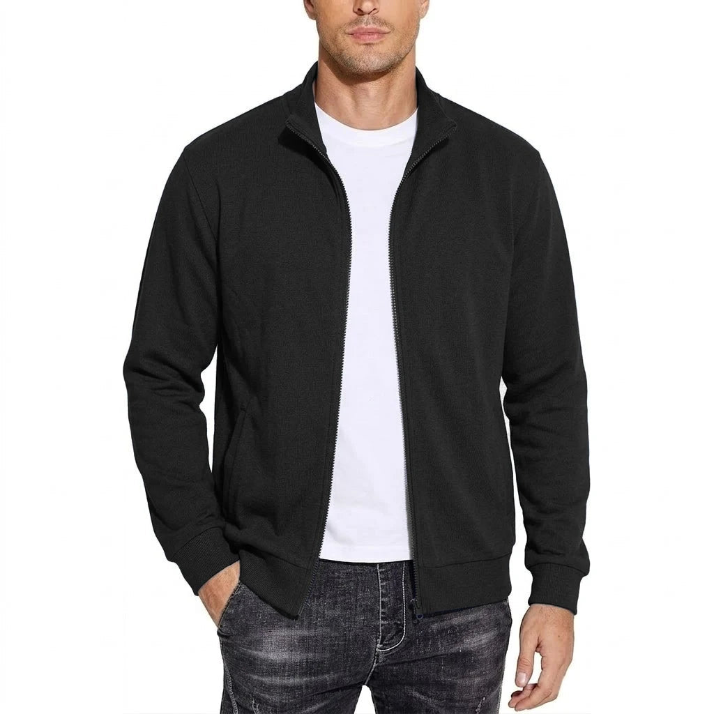 Man wearing the black zip-up jacket open over a white t-shirt, with stand collar, ribbed cuffs and a hand in the pocket. 1