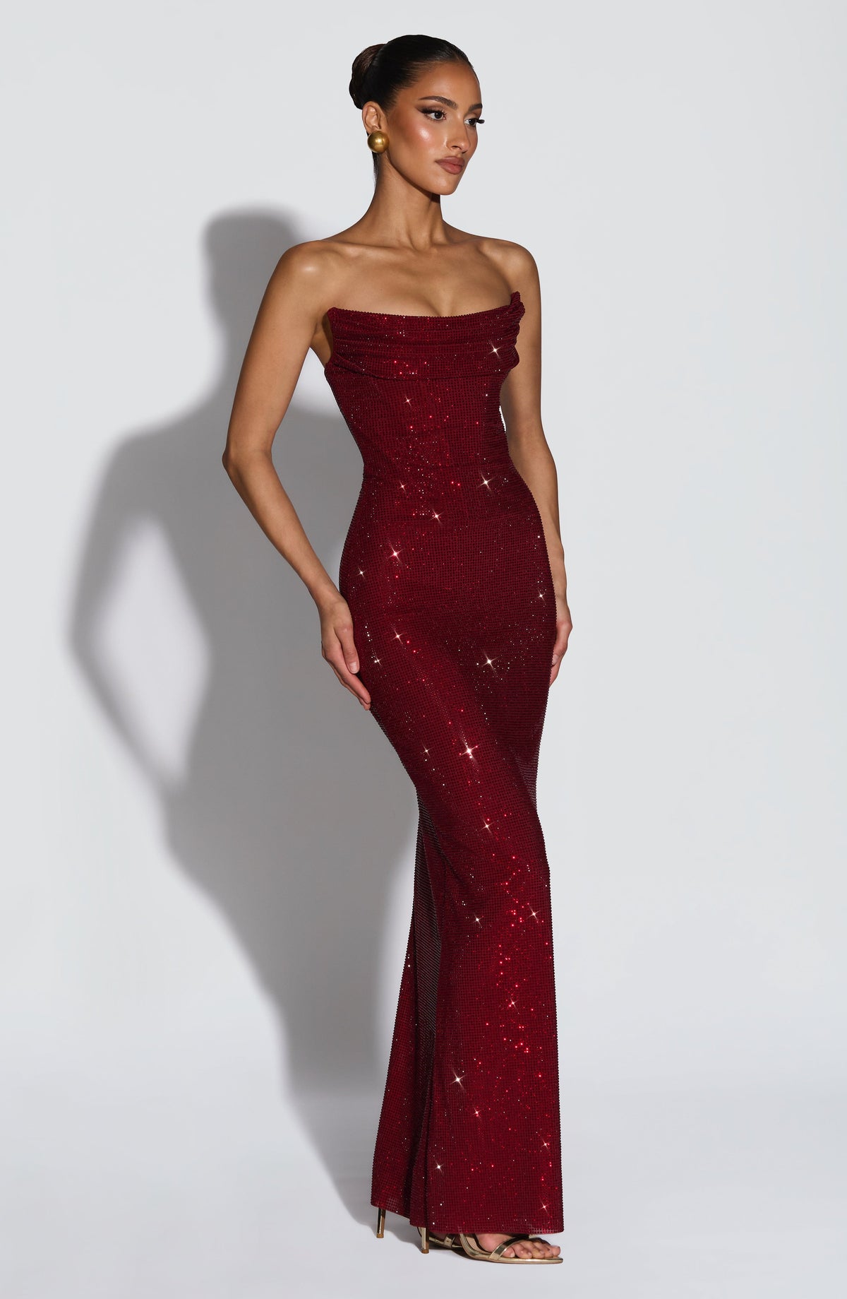 Three-quarter view of the burgundy strapless gown, model turned slightly, showing the fitted shape down to the floor. 4