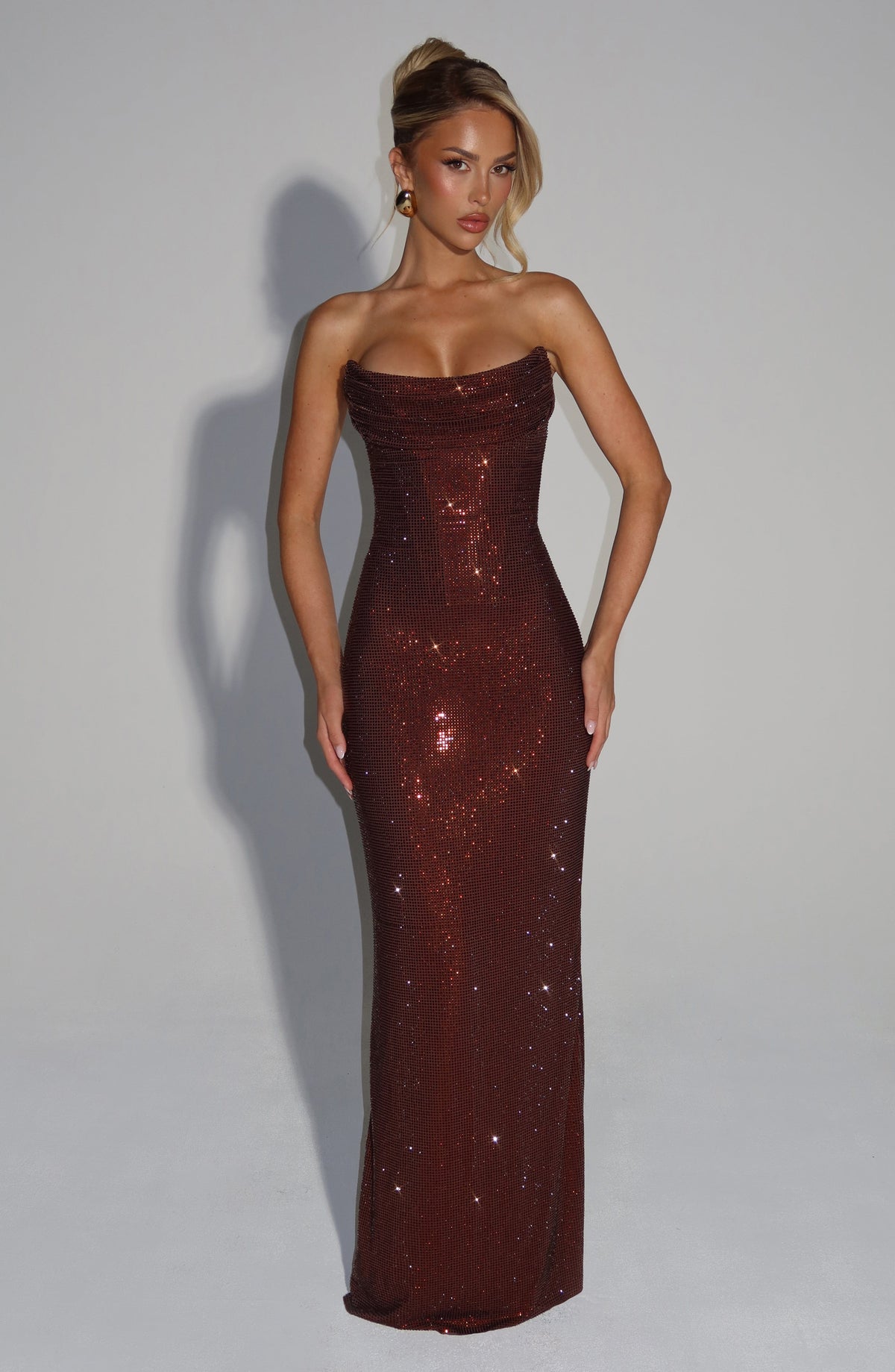 Blonde model facing front in the strapless brown rhinestone mesh maxi dress with draped neckline, hands resting at her hips. 5