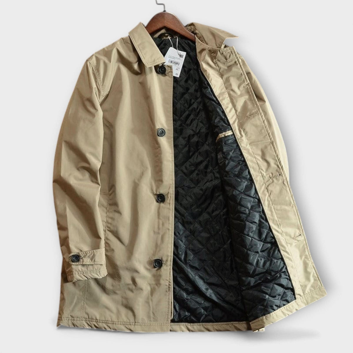Beige coat hanging with its front open, showing the quilted black lining, black buttons, collar and cuff tab. 7