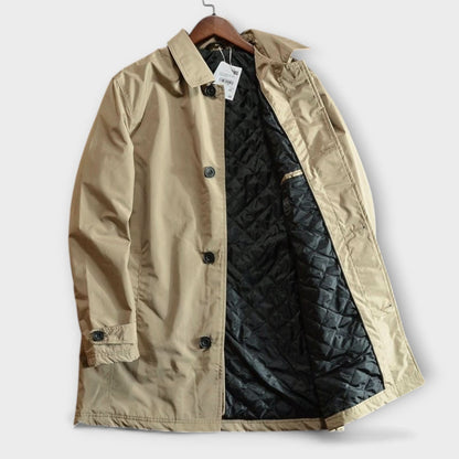 Beige coat hanging with its front open, showing the quilted black lining, black buttons, collar and cuff tab. 7