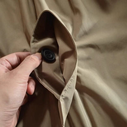 Close-up of a hand holding open a beige coat pocket, with a black four-hole button inside. 8