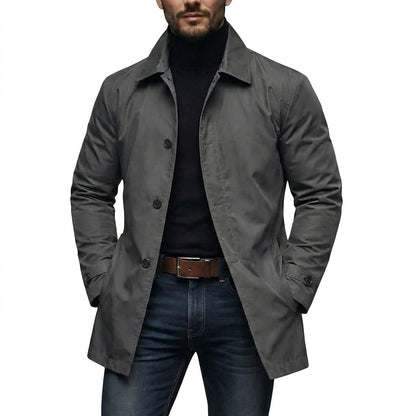Model wearing the grey coat open over a black roll-neck jumper, jeans and brown leather belt, hands in pockets. 1