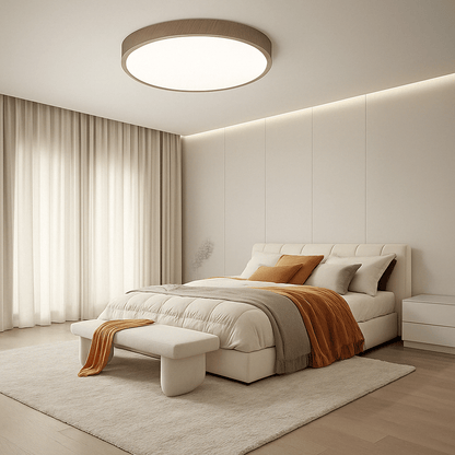 Wood-rimmed round ceiling light above a cream bedroom with a bench, soft rug and orange throws. 12