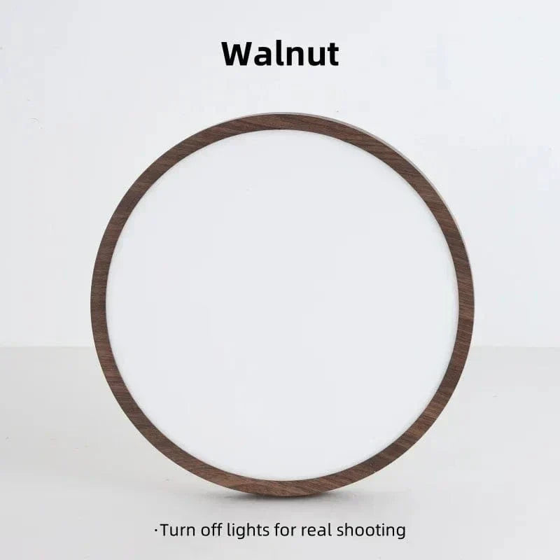 Walnut-finish round light stood upright against a plain wall, switched off, showing its white diffuser and wood-effect rim. 17