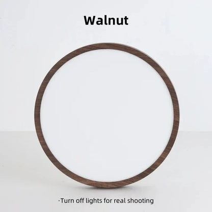 Walnut-finish round light stood upright against a plain wall, switched off, showing its white diffuser and wood-effect rim. 17