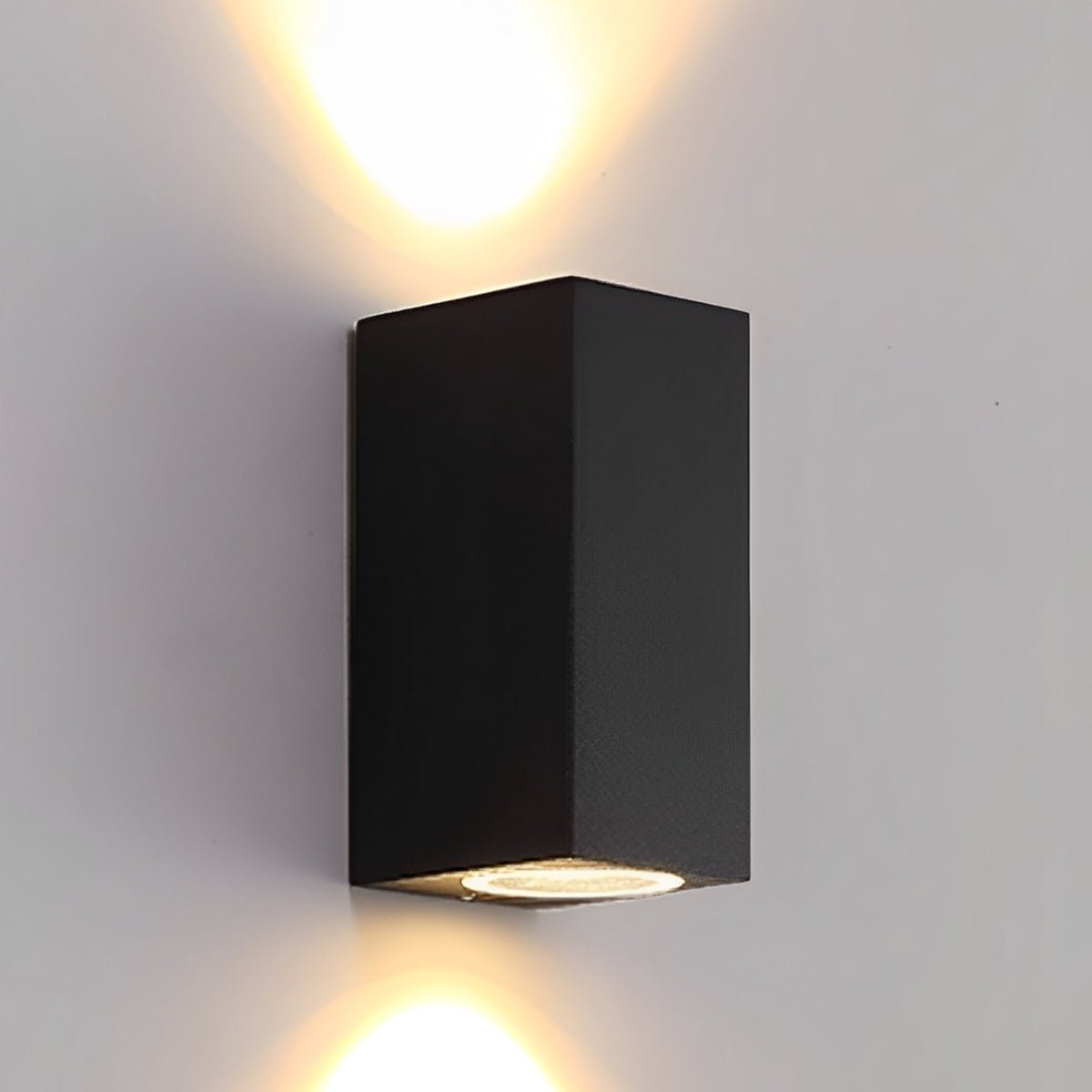 Tall black rectangular wall lamp projecting warm light both up and down a pale wall 3
