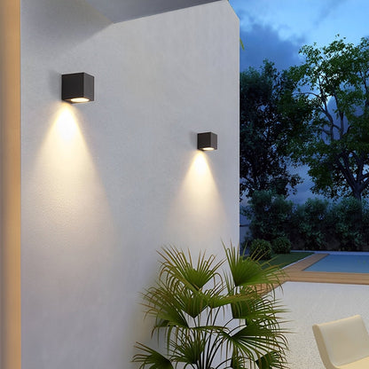 Two black cube wall lights casting downward beams on a white courtyard wall beside a pool 5