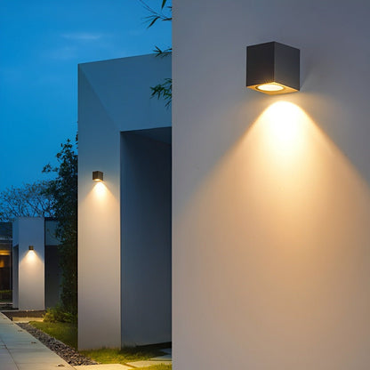 Black downlight wall lamp on a white wall, with more lights lining a pathway beyond 6
