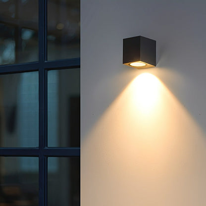 Black square wall lamp shining warm light downward beside a dark-framed window 11