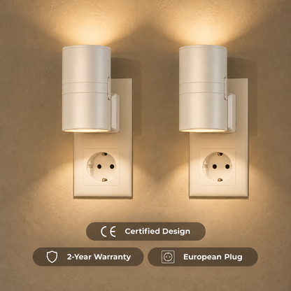 Pair of white cylindrical plug-in wall lights casting warm light up and down from sockets 2