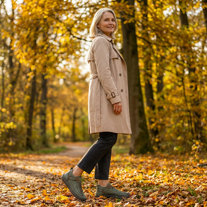 Woman in a trench coat walking through golden autumn woodland, wearing green lace-up trainers with a dark sole. 19