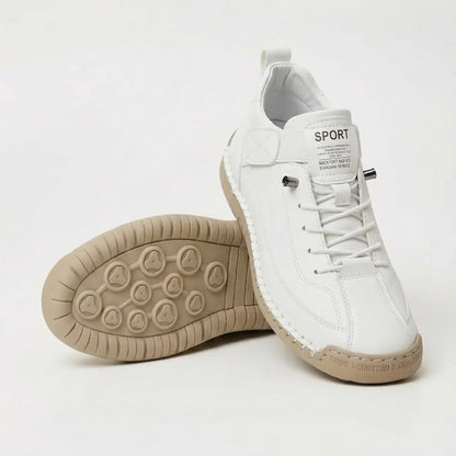 White lace-up trainers with elastic laces and hand-stitched edging, one shoe resting on its side to show the beige studded sole. 2