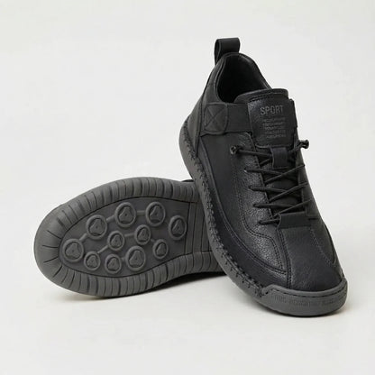 Black textured lace-up trainers with dark grey sole, one shoe angled upright and the other showing the circular tread pattern. 3