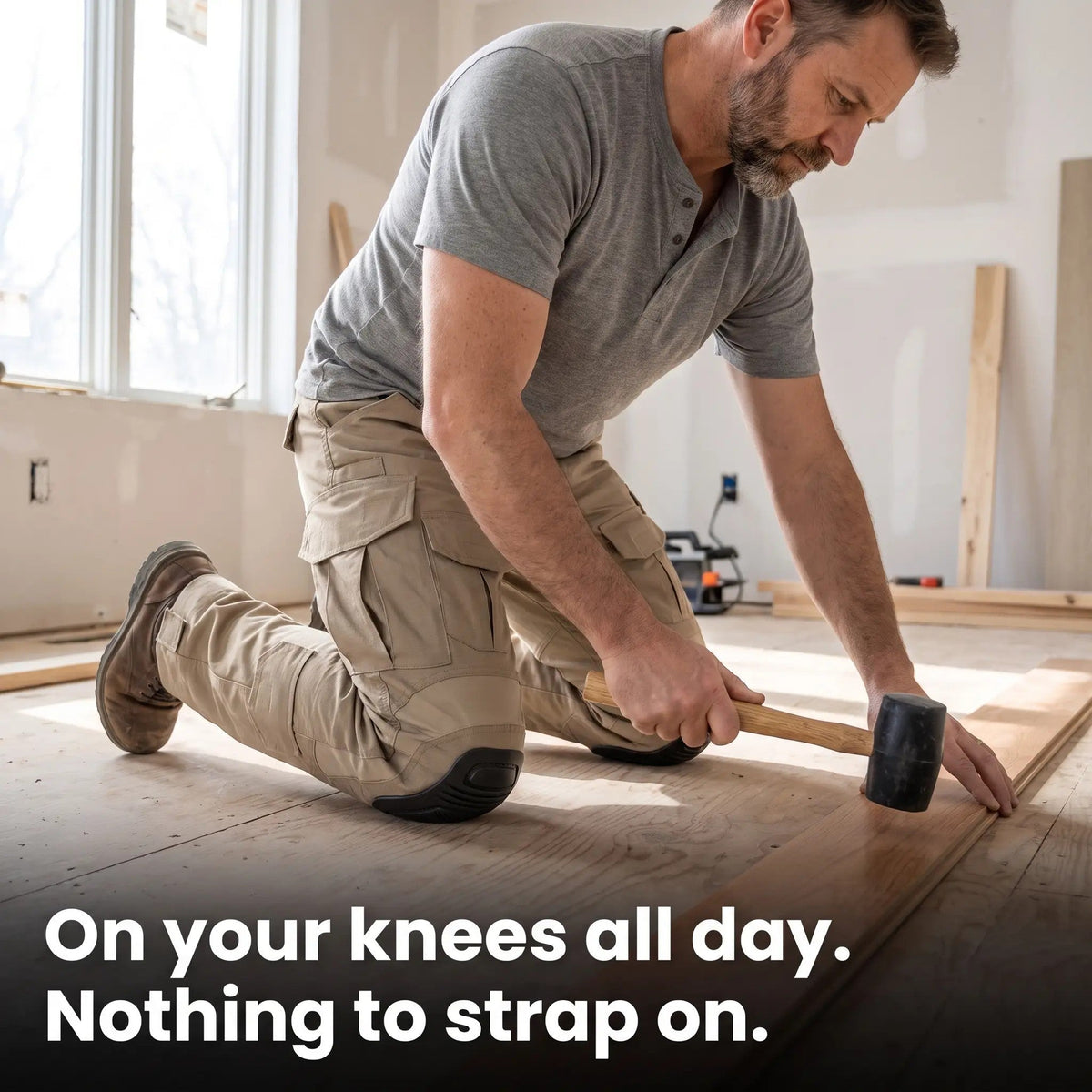 Man in beige cargo trousers kneeling on a bare floor, hammering a floorboard, with the knee pad taking his weight. 3