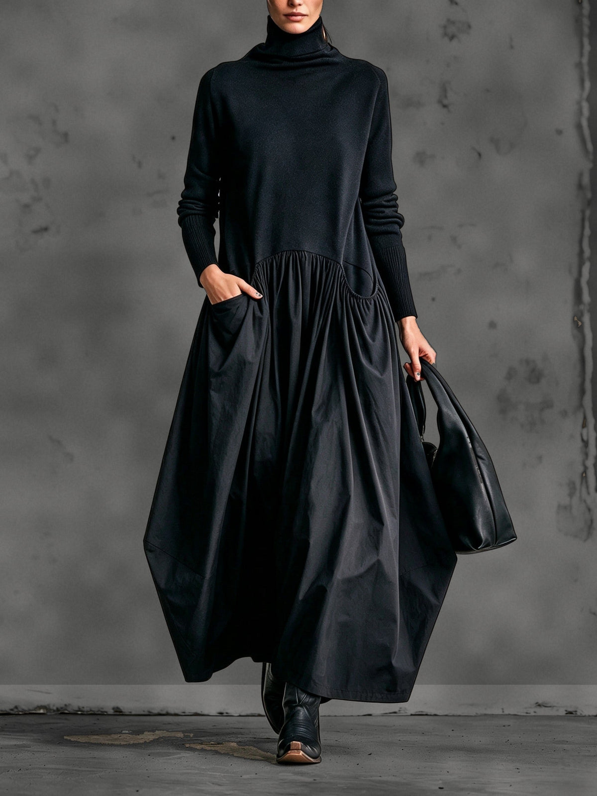 Model wearing the black long-sleeved maxi dress from the front, one hand in the pocket, carrying a bag 1