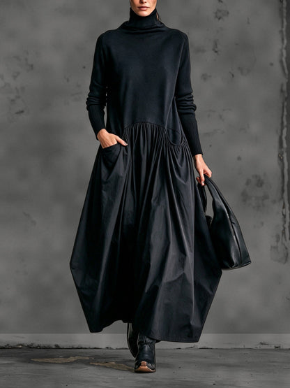 Model wearing the black long-sleeved maxi dress from the front, one hand in the pocket, carrying a bag 1