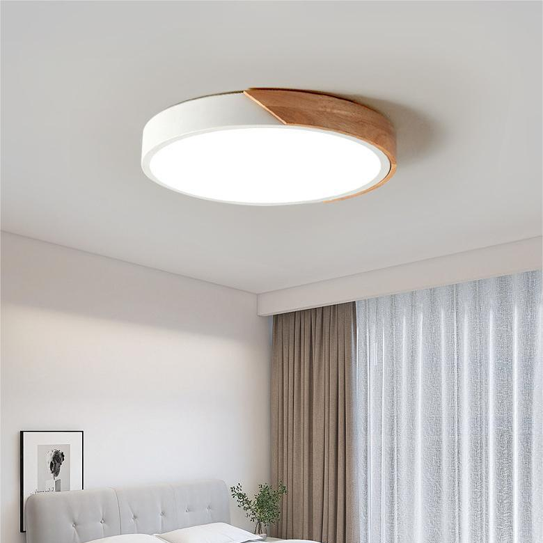White round ceiling light with a wooden segment on the edge, switched on in a bedroom with curtains and a grey headboard. 3