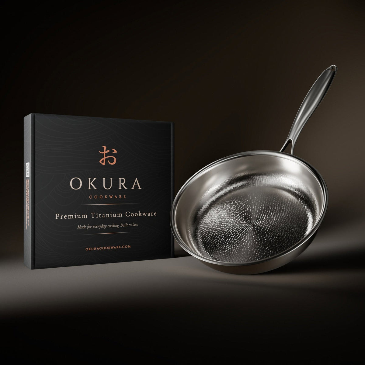 Frying pan tilted beside its black presentation box, showing the hammered interior and long handle against a dark backdrop. 9