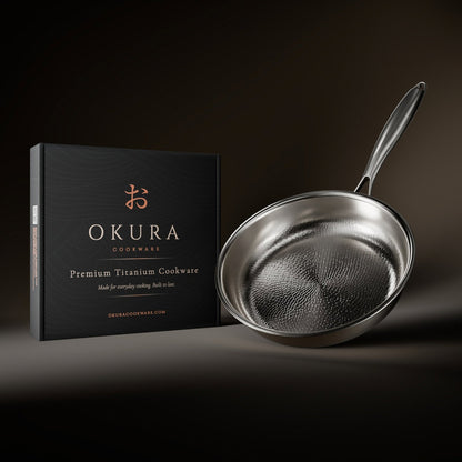 Frying pan tilted beside its black presentation box, showing the hammered interior and long handle against a dark backdrop. 9