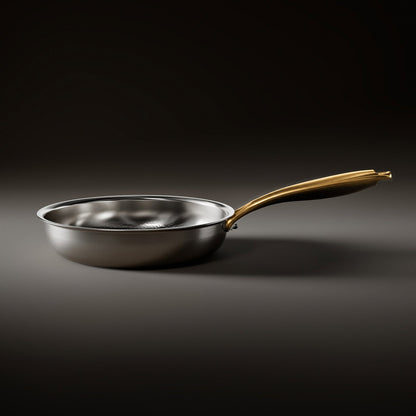 Side view of the frying pan resting flat, showing its low polished steel wall and the long brushed gold handle. 2