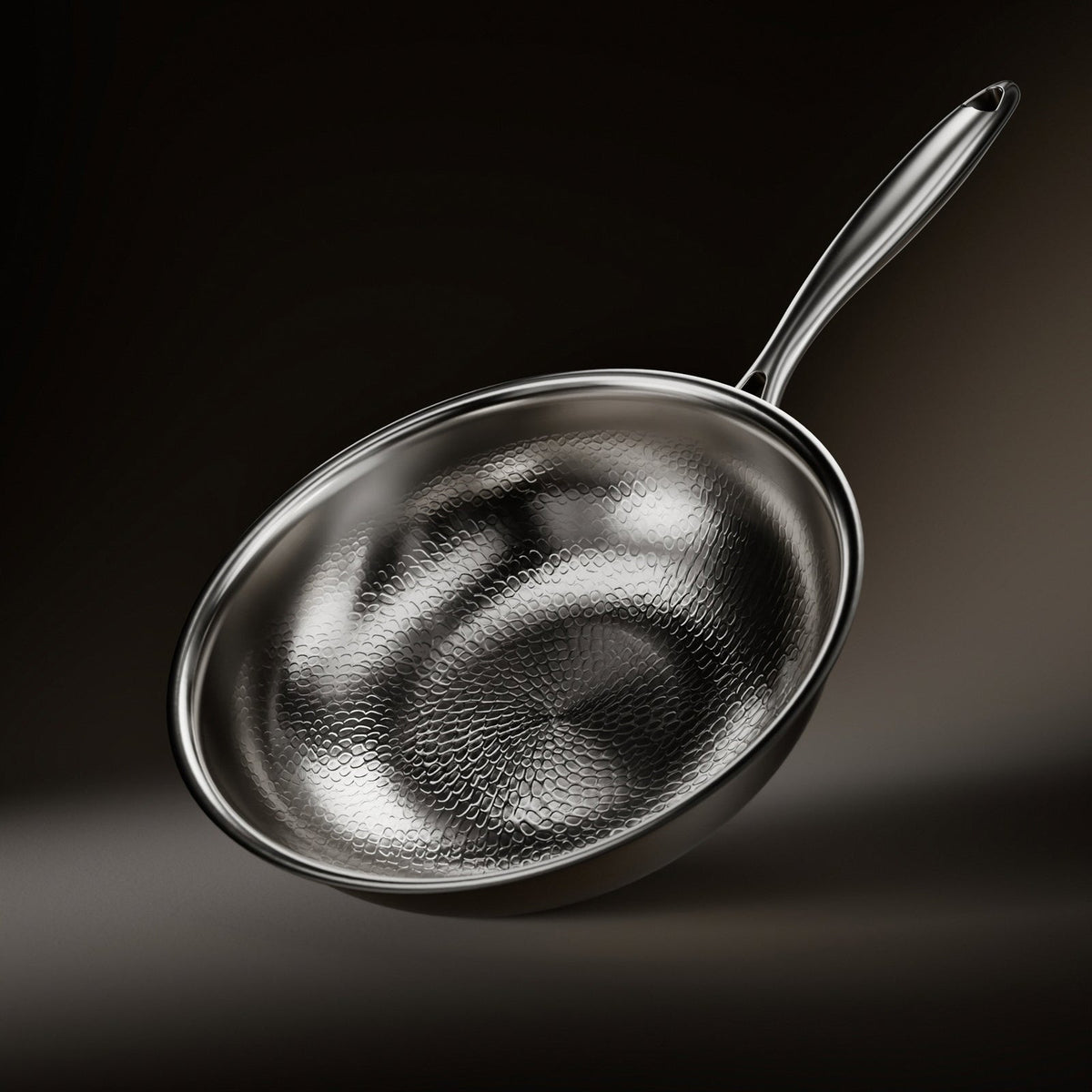 Wok pan tilted on a dark background, showing its hammered, scale-like textured interior and a long polished metal handle. 1