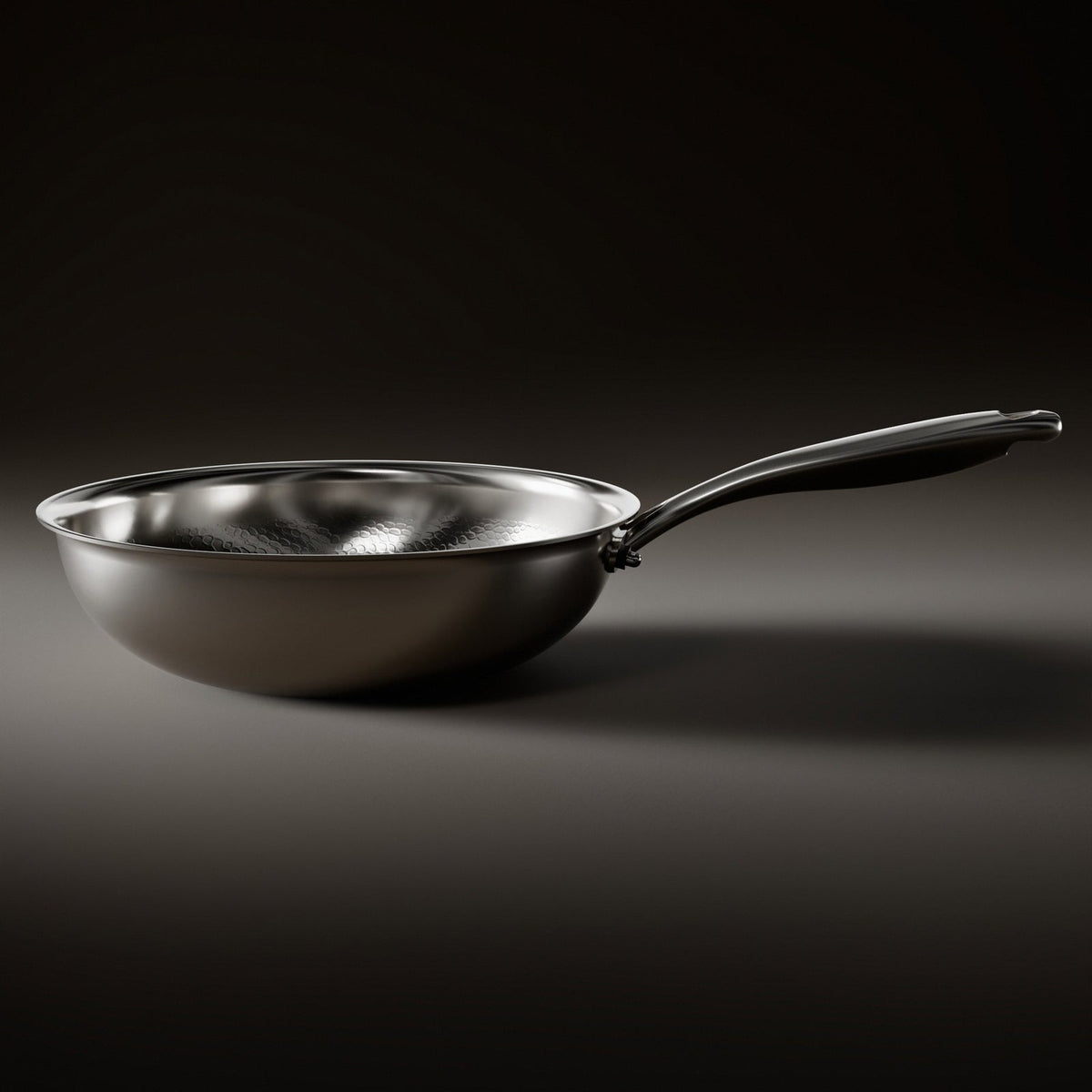 Side view of the wok pan resting on a dark surface, showing its smooth rounded outer body, flat base and long handle. 2