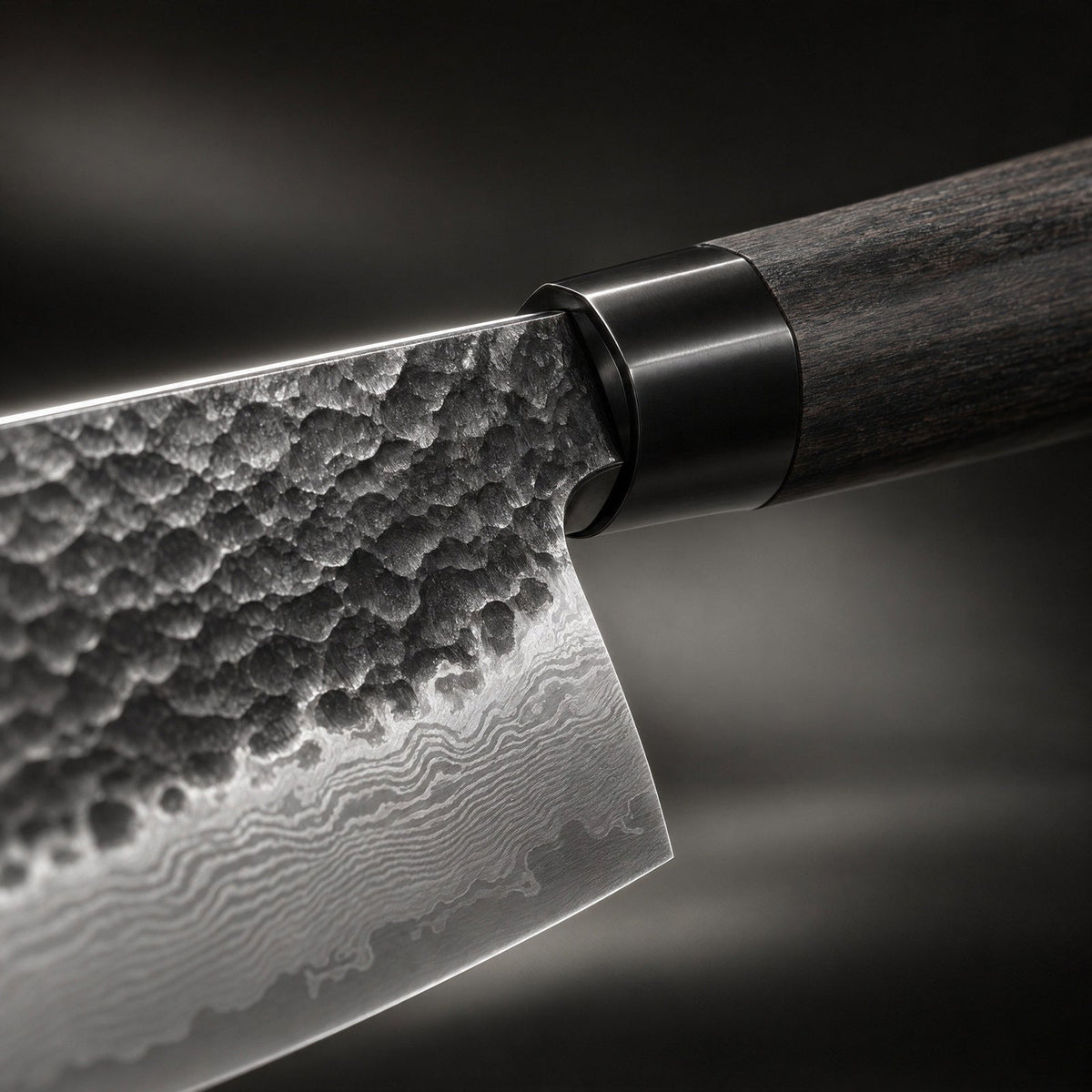 Close-up of the blade where it meets the handle, showing the textured hammered surface, wavy layered-steel pattern, black metal collar and dark wood. 3